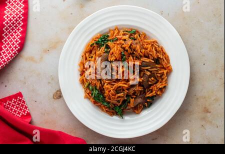 Vegetarische Reisjollof mit Pilzen und Grünkohl auf einer weißen Schüssel mit roter Serviette. Stockfoto