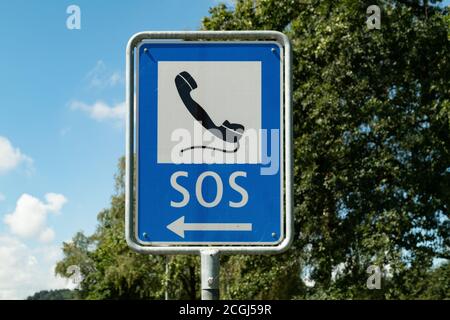 Notrufzeichen mit schwarzem Telefon auf weiß-blauem Hintergrund vor blauem Himmel und grünem Wald gemalt, Notrufe sind wichtig, um Leben zu retten, Stockfoto