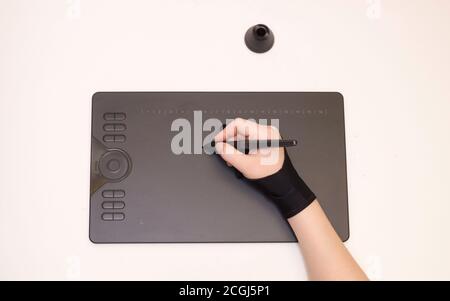 Die Hand einer Frau in einem speziellen Handschuh zeichnet sich durch eine grafische Tablette, weißen Hintergrund, isoliert. Draufsicht, Werkzeuge für grafische Zeichnung. Stockfoto