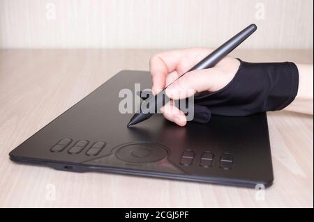 Die Hand einer Frau in einem speziellen Handschuh zeichnet sich durch ein Grafiktablett aus. Seitenansicht, Werkzeuge für grafische Zeichnung. Stockfoto