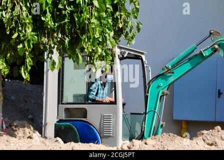 Bauarbeiter mit Maske Betrieb der Planierraupe auf der Baustelle während Covid-19 Pandemie-Ära. Covid-19-Inhalt Stockfoto