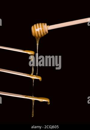 Zuckerpaste oder Schönheitswachs zum Zuckern fließt von einem hölzernen Dipper zu hölzernen Spateln. Haarentfernung, Enthaarung. Schwarzer Hintergrund, freier Platz für Text. Stockfoto