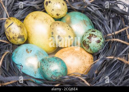 Ostereier im Nest sind aus nächster Nähe. Goldene und blaue Farben, Wachtel und Hühnereier. Frohe Ostern! Stockfoto