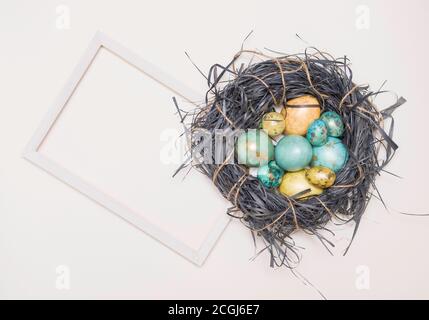 Ostereier in einem Nest und einem weißen Textrahmen. Auf weißem Hintergrund. Goldene Farben, Frohe Ostern. Draufsicht, flach. Stockfoto