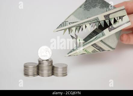 Eine Origami-Figur von Dollar in Form eines Tierkopfes mit Zähnen und einer Rubel-Münze. Das Konzept des Wachstums des Dollars gegenüber dem Rubel. Stockfoto