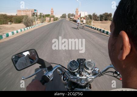 Ein arabischer ägyptischer Mann, der mit seinem Motorrad durch das Dorf Al Qasr in der Oase Dakhla in der westlichen Wüstenregion, im New Valley, Ägypten, fährt. Stockfoto