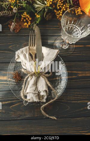 Thanksgiving-Dinner-Tisch. Stilvoller Teller mit Besteck und Herbstdekorationen, Kürbis, Naturzweigen und Herbstblumen auf rustikalem Tisch. Stockfoto