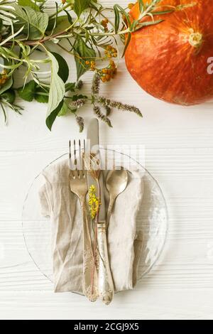 Umweltfreundliches Thanksgiving-Fest. Stilvoller Teller mit Besteck und Herbstdekorationen, Kürbis, Naturzweigen und Herbstblumen auf weißem Tisch. Rus Stockfoto