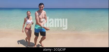 Panoramablick auf lächelnde Mann und Frau romantischen Paar im Urlaub zu Fuß auf einem einsamen tropischen Strand mit klaren blauen Himmel Panorama-Web-Banner. Stockfoto