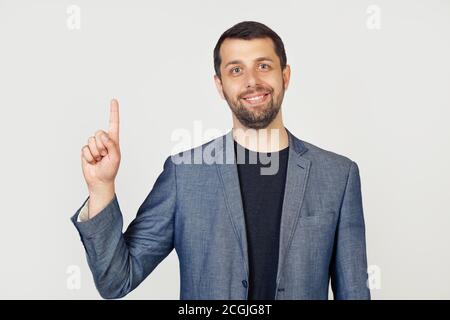 Junger Geschäftsmann Mann mit Bart lächelnd, zeigt Nummer eins mit den Fingern auf der Hand, lächelt selbstbewusst und glücklich, Blick in die Kamera. Der Mann zeigt einen Finger. Nummer 1. Stockfoto