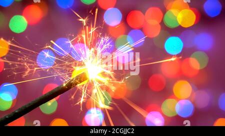 Hell brennender Funkler vor dem Hintergrund der entkochten bunten Girlande. Unscharfer Hintergrund. Frohe Weihnachten oder Geburtstagsfeiertage Konzept. Schließen-U Stockfoto