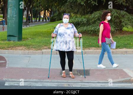 Huelva, Spanien - 10. September 2020: Übergewichtige kaukasische Frau, die mit Nordic Walking Stöcken geht und eine schützende Gesichtsmaske trägt, die durch Coronavirus covid verursacht wird Stockfoto