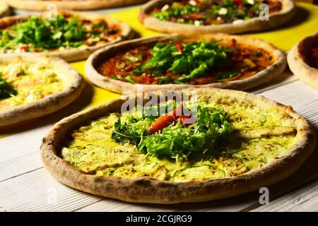 Pizzakreise mit Fleisch, Zucchini, Salat und Käse auf Holzhintergrund. Italienische Pizza und Pizzeria Konzept. Verschiedene Pizzabücken für die Speisekarte. Nehmen Sie Lebensmittel mit verschiedenen Zutaten und knackigen Kanten Stockfoto