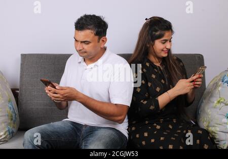 Indisches Paar mit Smartphone / Handy auf dem Sofa sitzen. Stockfoto