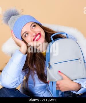 Perfektes Lächeln. Grippe und kalte Jahreszeit. Ledertasche Mode. Warme Winterkleidung. Shopping. Frohe Winterferien. Mädchen in Puffmantel. Kunstpelzmode. Frau in Mütze Hut mit Rucksack. Stockfoto