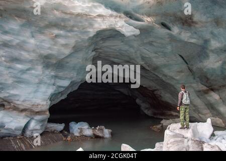 Ein Mann steht im Schnee vor dem Eingang Zur Schneehöhle des Alibek-Berggletschers Dombay mit hohen Mauern aus gefrorenem Schnee Stockfoto