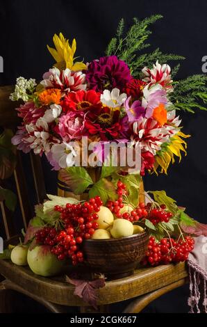 Herbst stimmungsvolles Stillleben mit einem bunten schönen Bouquet von Gartenblumen, roten Beeren, Äpfeln, Herbstblättern auf schwarzem Hintergrund. Stockfoto