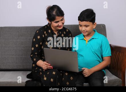 Coronavirus-Ausbruch und Bildungskonzept - Sperrung und Schulschließungen. Indische Mutter hilft Sohn studieren Online-Klassen zu Hause. COVID-19 Stockfoto