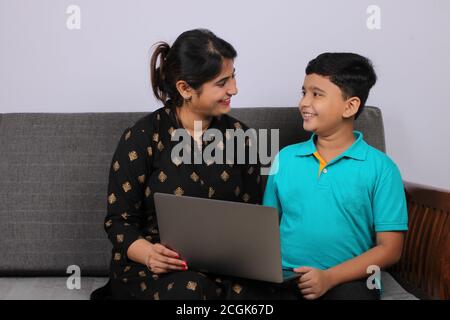 Coronavirus-Ausbruch und Bildungskonzept - Sperrung und Schulschließungen. Indische Mutter hilft Sohn studieren Online-Klassen zu Hause. COVID-19 Stockfoto