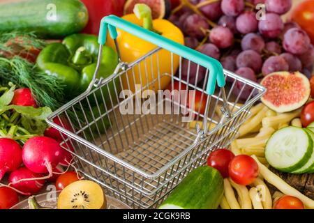 Leerer Warenkorb. Viel Essen, Gemüse und Obst in der Umgebung. Das Konzept von steigenden Preisen, Inflation und teureren Lebensmitteln Stockfoto