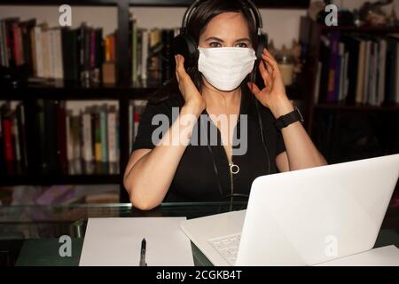 Frau, die sich auf den Klang von Hörgeräten in einem konzentriert Büro in Mexiko-Stadt, während sie Mundschutz trägt Ansteckung durch eine Covid 19 Pfanne verhindern Stockfoto