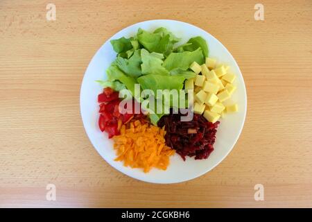 Draufsicht auf einen gesunden, selbstgemachten vegetarischen proteinreichen Salatteller mit grünem Salat, geriebenen Karotten und Rote Beete sowie gehackten Tomaten und Käse Stockfoto