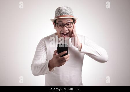 Attraktive junge asiatische Mann lesen SMS chatten auf seinem Handy, schockiert überrascht Ausdruck Stockfoto
