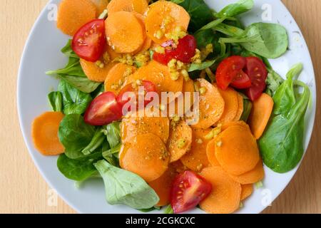 Luftaufnahme eines gesunden vegetarischen hausgemachten Salats mit Nusssalat oder Lammsalat, Karottenscheiben, Tomaten und Knoblauch auf einem weißen Teller Stockfoto