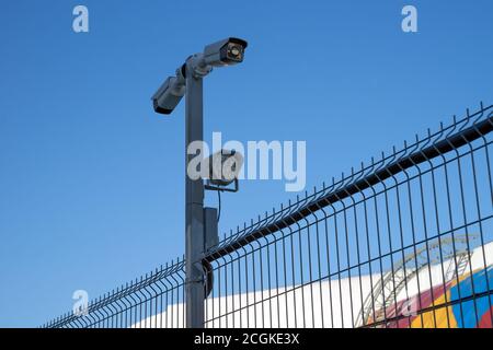 Die Überwachungskamera ist am Metallzaun des geschützten Bereichs im Hintergrund des Himmels befestigt. Stockfoto