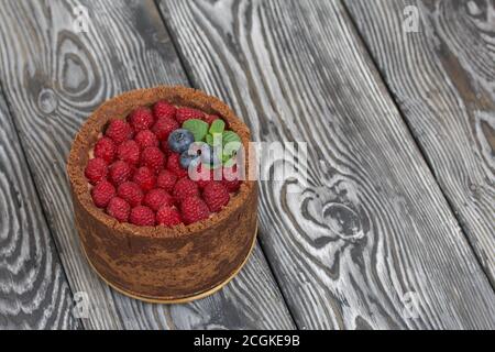 No-Bake Schokoladenkuchen mit Frischkäse. Garniert mit Himbeeren, Heidelbeeren und Minzblättern. Auf der Oberfläche von Kiefernplatten in schwarz und lackiert Stockfoto