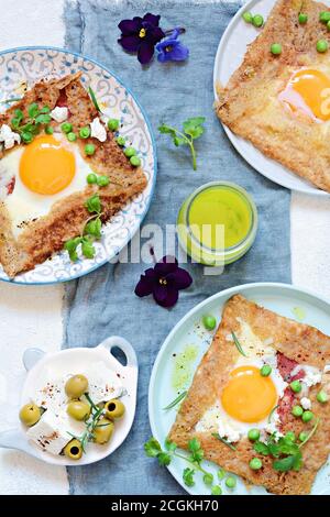 Bretonische traditionelle Pfannkuchen aus Buchweizenmehl mit Schinken, Käse, Ei, Feta, grüne Erbsen und grüne Butter. Frühstück von Buchweizen dünne Pfannkuchen wi Stockfoto