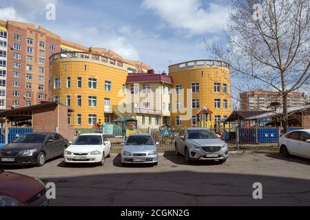 Das Gebäude des Kindergartens in einem Wohnviertel der Stadt Krasnojarsk mit geparkten Autos davor, vor dem Hintergrund eines resi Stockfoto