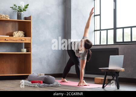Junge Frau, die Yoga praktiziert, dabei rotierte Dreieck Pose, Parivrrta Trikonasana Stockfoto