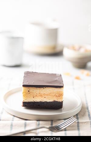 Stück Kuchen mit Soufflevogelmilch, Keks, Mousse und dunkler Schokolade auf einem weißen Teller, hellem Hintergrund Stockfoto