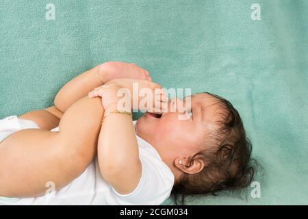 6 Monate altes Baby Mädchen auf dem Rücken beißen eigenen Zehen, Nahaufnahme Stockfoto