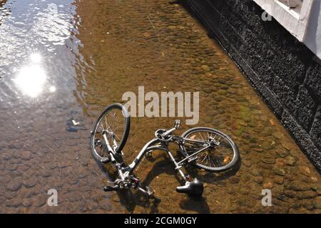 In fließendem Wasser des Freiburger Kanals mit Spiegelung der Mittagssonne ist ein Skelett eines Bikes schwer beschädigt nicht mehr für den Einsatz geeignet. Stockfoto