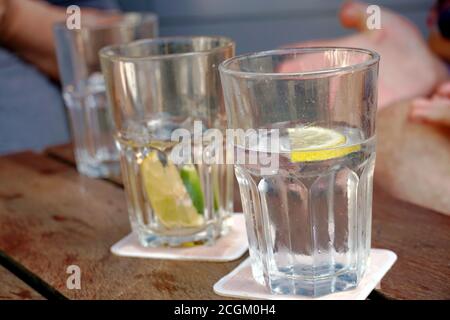 Gläser mit Wasser, Zitronen- und Limettenscheiben auf einem Tisch in einem Restaurant im Freien. Die Gläser werden an einem heißen Sommertag beschlagen oder gedämpft. Stockfoto