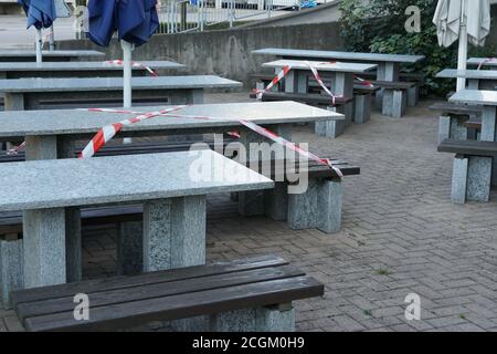 Verlassene Restaurant mit rot-weißem Sperrband, das als neue Normalität jeden zweiten Tisch sichert, um soziale Distanz zu halten. Stockfoto