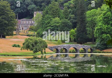 St. Peter's Church, das Bristol High Cross und die Palladian Bridge von der anderen Seite des Sees auf dem Stourhead Estate, in der Nähe von Mere, Wiltshire, England Stockfoto