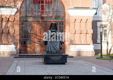 Denkmal für den Heiligen Luka Voyno-Jasenetsky vor dem Eingang zur Pfarrei des Tempels des Heiligen Johannes des Vorläufers (1890) im Herbst. Stockfoto