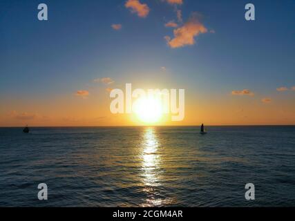 Schöner Sonnenuntergang mit großer gelber Sonne über der Meeresoberfläche Und Silhouetten von zwei kleinen Booten Stockfoto