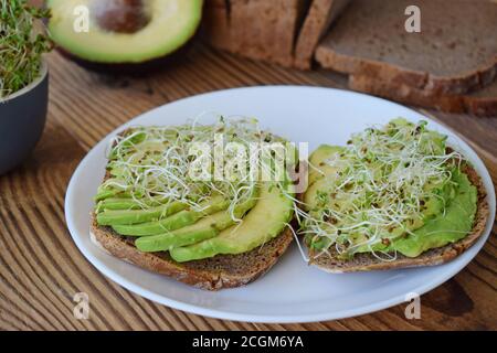 Frisch zubereitetes vegetarisches Sandwich mit Vollkornbrot, Luzerne gekeimt und Avocado auf rustikalem Holztisch, Draufsicht. Gesunde Ernährung Hintergrund Stockfoto