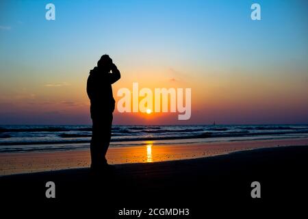 Der Mensch hat sich vor einem lebhaften Sonnenuntergang am Meer geschildet Stockfoto