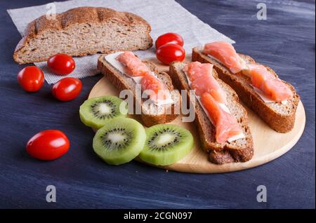 Sandwiches mit geräuchertem Lachs und Butter auf dunklem Holzhintergrund. Kirschtomaten. Nahaufnahme. Stockfoto