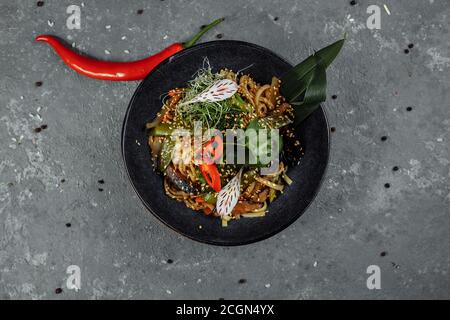 Gebratene Nudeln und Gemüse, in schwarzer Schüssel. Köstliche, nahrhafte asiatische Küche Stockfoto