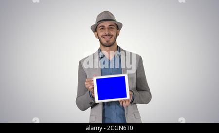 Casual Mann in einem Hut zu Fuß und zeigt digitale Tablette Zur Kamera Stockfoto