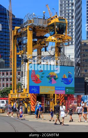 Tag der offenen Tür im Hafen von Auckland, Neuseeland. Ein riesiger Straddle-Träger, für das Bewegen von Transportbehältern, hält einen Videoschirm hoch Stockfoto