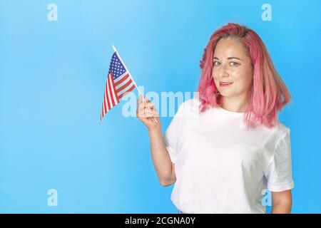 Junge Studentin hält amerikanische kleine Flagge und lächelt auf blauem Hintergrund, glückliche Frau hält USA Flagge. Englisch lernen. Studieren im Ausland, international l Stockfoto