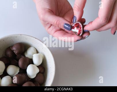 Die Hand der Frau wählt und greift frisch rot und glänzend frisch Himbeeren in hausgemachte schwarze und weiße Schokolade getaucht Stockfoto