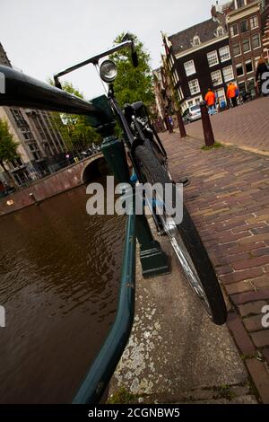 Ein abstraktes geneigtes Bild, das eine Nahaufnahme eines alten Oldtimer-Motorrads zeigt, das an einem grünen Metallgeländer einer Brücke in Amsterdam festgebunden ist. Der Kanal, Ziegel sid Stockfoto
